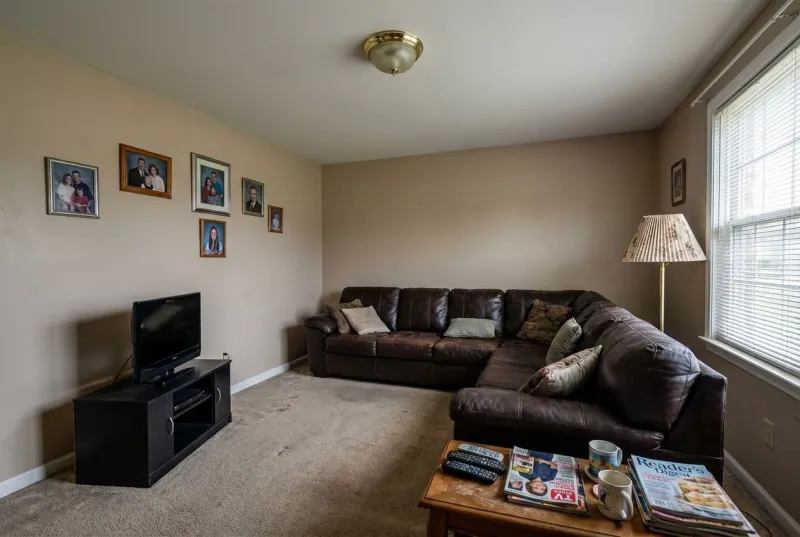 Dated American living room being scanned by Deqor AI agent - detecting design issues like cheap fixtures, worn carpet, dated furniture, and poor wall decor